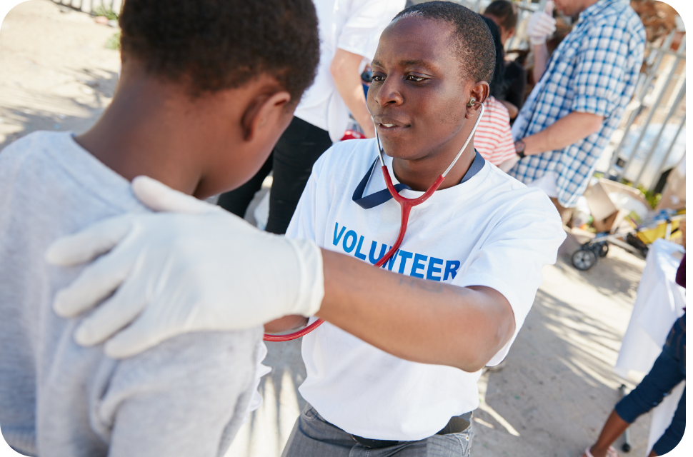 Volunteer in white shirt placing gloved hand on a boy's shoulder, outdoor photo