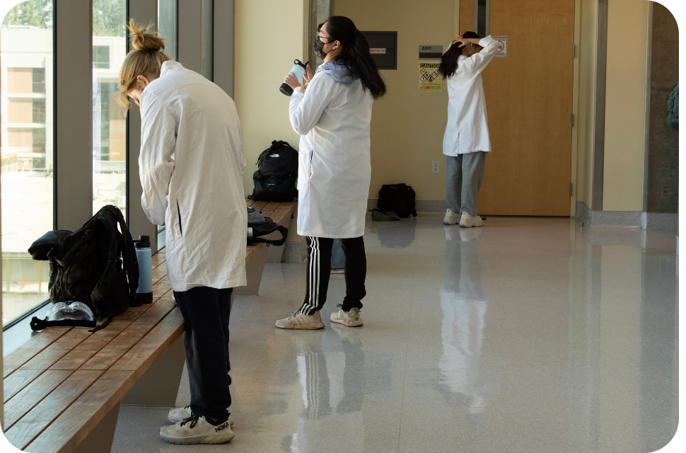 Three people in white lab coats taking photos in a bright hallway
