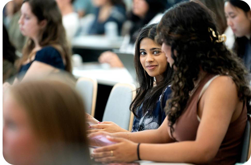 Two students talking in a lecture hall, one smiling and looking toward the viewer