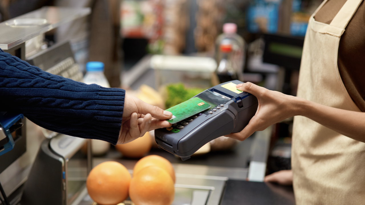 Customer tapping smartphone to card reader at grocery checkout, peaches on conveyor