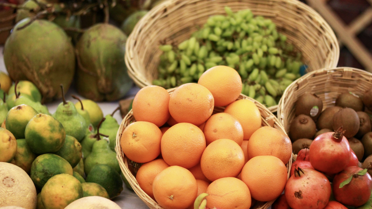 Basket of ripe oranges surrounded by coconuts, green grapes, limes and pomegranates