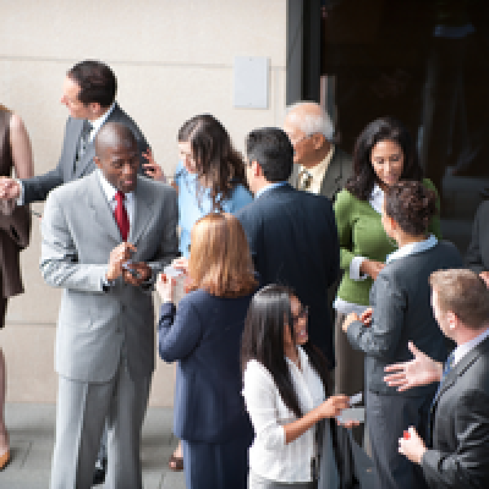 Diverse professionals in suits networking outside a building, chatting and exchanging cards.