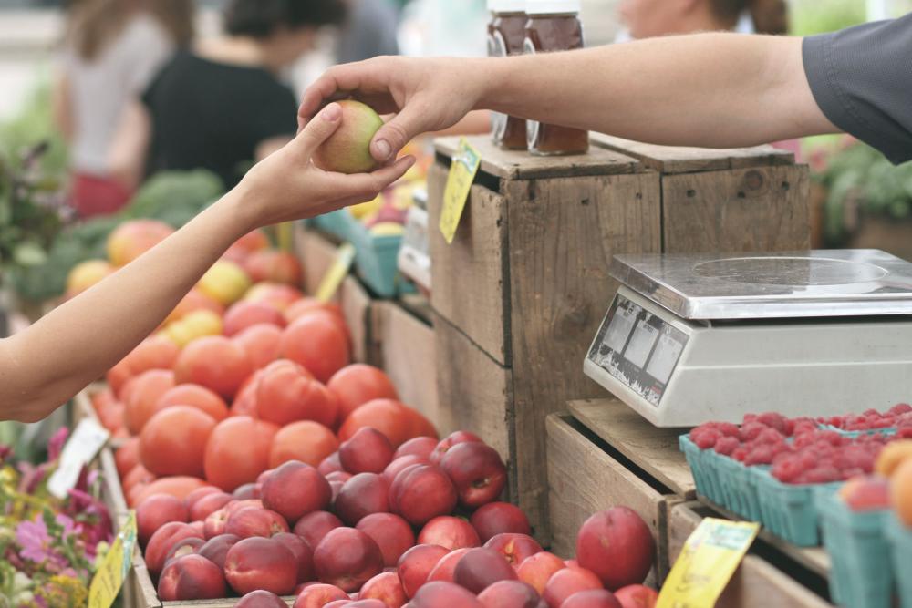 Hand giving lemon to child at a farmers market stall with crates of fruit
