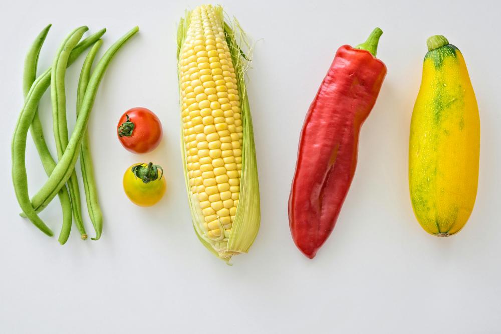 Fresh vegetables lined horizontally: green beans, two tomatoes, corn, red pepper, yellow squash