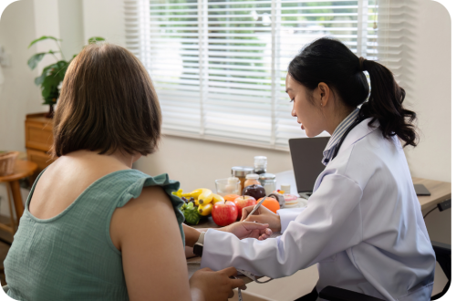 Female doctor consulting a patient at a desk by a sunny window with fruit