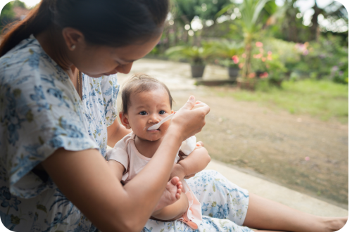 Mother feeding baby with spoon on her lap outdoors