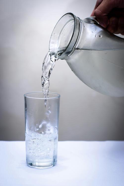 Hand pouring water from a glass pitcher into a tall glass, bubbles forming