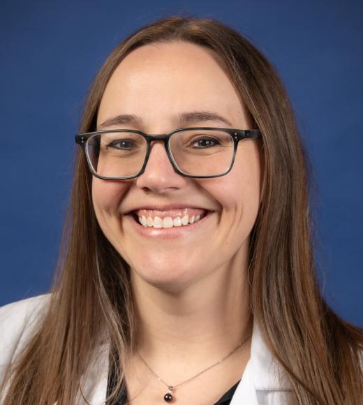 Headshot of smiling woman with glasses wearing UC Davis lab coat on blue background