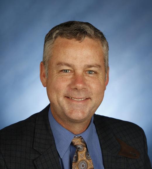 Smiling middle-aged man in suit and tie, blue backdrop, professional headshot
