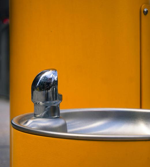 Stainless-steel drinking fountain on a bright yellow post, outdoor photo