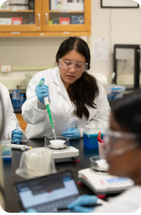 Woman scientist in lab coat, safety goggles and gloves pipetting at lab bench