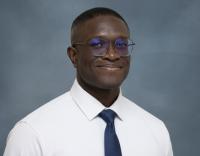 Professional headshot of smiling Black man in glasses, white shirt and navy tie