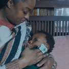 Woman cradling sleeping baby on bench in soft, intimate indoor scene
