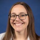 Headshot of smiling woman with glasses wearing UC Davis lab coat on blue background