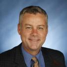 Smiling middle-aged man in suit and tie, blue backdrop, professional headshot
